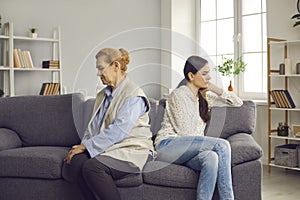 Offended older woman and her adult daughter are sitting on the couch with their backs to each other.