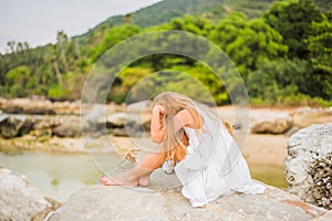 Offended sad girl with long hair sitting on a rock on the shore back