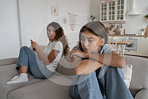 Offended teen girl feeling sad after argument with parent, sitting separately with mother on sofa