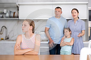 Offended teen girl listening to reprimand of displeased parents photo