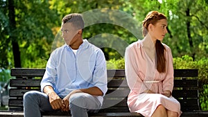 Offended teenagers sitting on bench turned from each other, misunderstanding