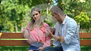 Offended woman listening to boyfriend explanations sitting park after quarrel