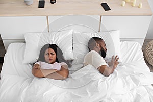 Offended young african american wife with crossed arms on chest, cant sleep with snoring husband on bed