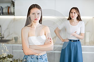 Offended young girl standing in the kitchen, angry mother talking