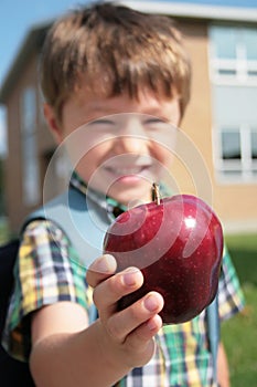 Joven niño sonriente que ofrece una manzana.