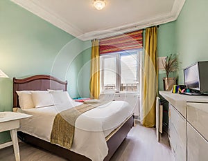 an office bedroom featuring a single bed with a headboard, a small window adorned with a Roman blind, a desk, and storage, all