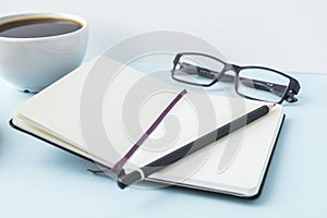 Office blue table with blank notepad, pencil, glasses and coffee cup. Copy space for text.