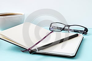 Office blue table with blank notepad, pencil, glasses and coffee cup. Copy space for text.