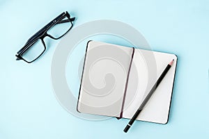 Office blue table with blank notepad, pencil, glasses. Copy space for text. Flat lay. Top view.