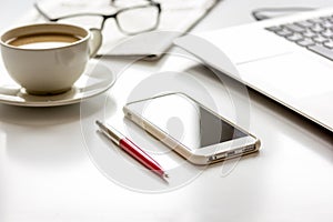 Office breakfast with coffee, phone and laptop on white desk photo