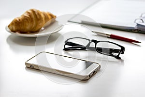 Office breakfast with croissant and phone on white desk photo