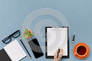 Office, business utensils on a blue table, telephone, a cup of tea, pencils, a notebook, glasses, a plant in a pot. Hand signing