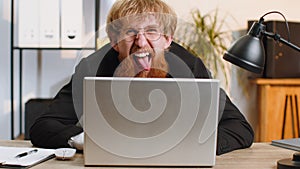 Office businessman hiding behind laptop computer making funny silly face fooling around, disrespect