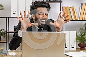 Office businessman hiding behind laptop computer making funny silly face fooling around, disrespect