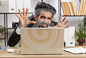 Office businessman hiding behind laptop computer making funny silly face fooling around, disrespect