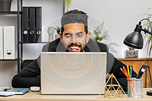 Office businessman hiding behind laptop computer making funny silly face fooling around, disrespect