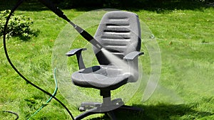 Office chair cleaning under strong water stream on green grass