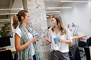 Office coffee break with two business female colleagues having fun chatting over cups of coffee