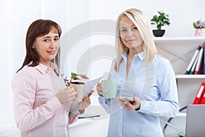 Office coffee break. Two female colleagues with cups of coffee talking.