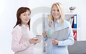 Office coffee break. Two female colleagues with cups of coffee talking.