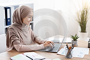 Focused arabic businesswoman in hijab working on laptop computer in office photo