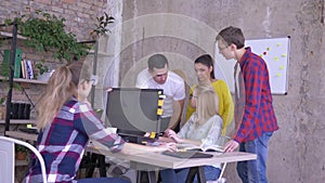 Office coworkers standing at table with laptop discussing business plan and creative ideas