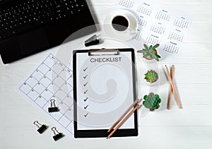 Office desk business table with laptop, blank paper checklist, calendar, eyeglasses, cup of coffee and green plants on white