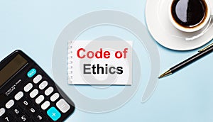 An office desk with a cup of coffee, a calculator, a pen and a blank notebook with the text of the CODE OF ETHICS. Place the