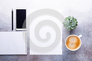 Office desk with cup of coffee, note pad, smartphone and blank paper. Top view. Copy space