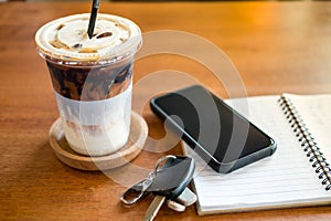 Office desk with cup of iced coffee and phone, car key on notebook