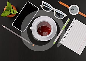 Office desk with a cup of tea, smartphone, wristwatch, notebook, pencil, glasses, potted plant. View from above. Template for