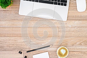 The office desk flat lay view with laptop, mouse, tree, black clip, heart latte coffee cup, notebook, pencil on wood texture