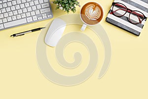 Office desk with keyboard computer, Pen, notebook, mouse, Cup of coffee on yellowbackground, Top view with copy space