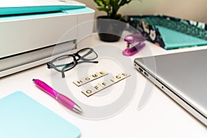 Office desk with laptop, printer, supplies and wooden block letters that say