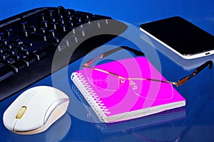 Office Desk with necessary accessories, blue background. On the desktop office notebook for important records, smartphone