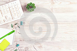Office desk table with computer keyboard,  notepad, pen, supplies  and green plant on light wood background