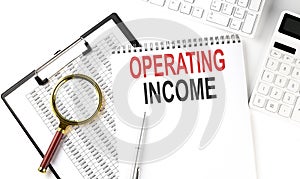 Office desk table with keyboard, notepad ,chart and calculator. Top view with text OPERATING INCOME