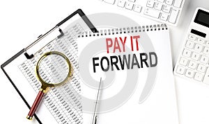 Office desk table with keyboard, notepad ,chart and calculator. Top view with text PAY IT FORWARD