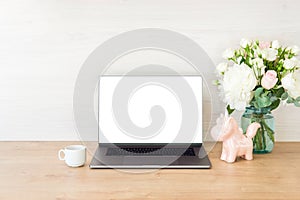 Office desk table with laptop computer with blank screen mockup, supplies, cup of coffee, flowers bouquet, unicorn on wooden