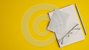 Office desk table with notebook, paper envelope, glasses and pencil on yellow background. Top view with copy space, flat lay.