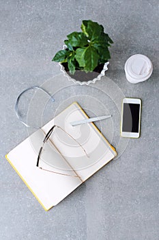 Office desk table with notebook planner, smart phone, glasses, coffee tree and coffee cup. Top view with copy space.