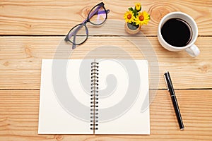 Office desk table with smartphone, pen on notebook, cup of coffee and flower. Top view with copy space (selective focus)..