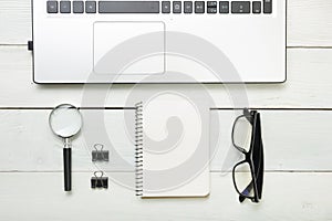 Office desk table with supplies. Top view. Copy space for text. Laptop, blank notepad, and magnifying glass