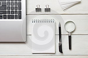 Office desk table with supplies. Top view. Copy space for text. Laptop, blank notepad, pen and magnifying glass