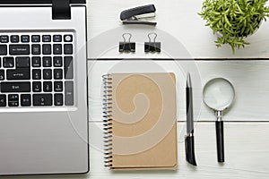 Office desk table with supplies. Top view. Copy space for text. Laptop, blank notepad, pen, magnifying glass and flower.