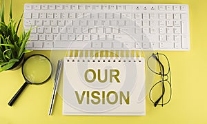 Office desk table Top view with keyboard and notebook text OUR VISION on the yellow background