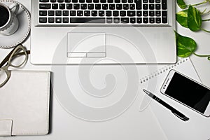 Office desk table top view and supplies, laptop, cup of black coffee, glasses, plant, cellphone on white background.