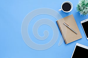 Flat lay top view mockup photo of working space with tablet, phone, coffee cup and notebook on blue pastel background.