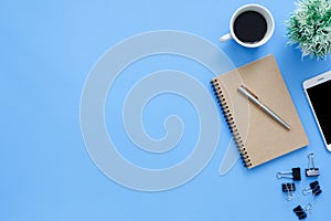 Flat lay top view mockup photo of working space with tablet, phone, coffee cup and notebook on blue pastel background.