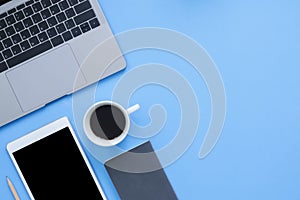 Flat lay top view mockup photo of working space with laptop, smartphone, coffee up and notebook on blue pastel background.